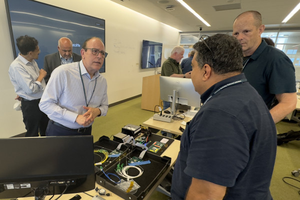 A crowd of people stand in a conference room next to a computer hardware. 