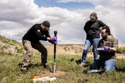 Three people digging into the ground with a core sampler