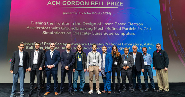 12 people standing on a stage in front of a screen with an image honoring the 2022 winners of the ACM Gordon Bell Prize.