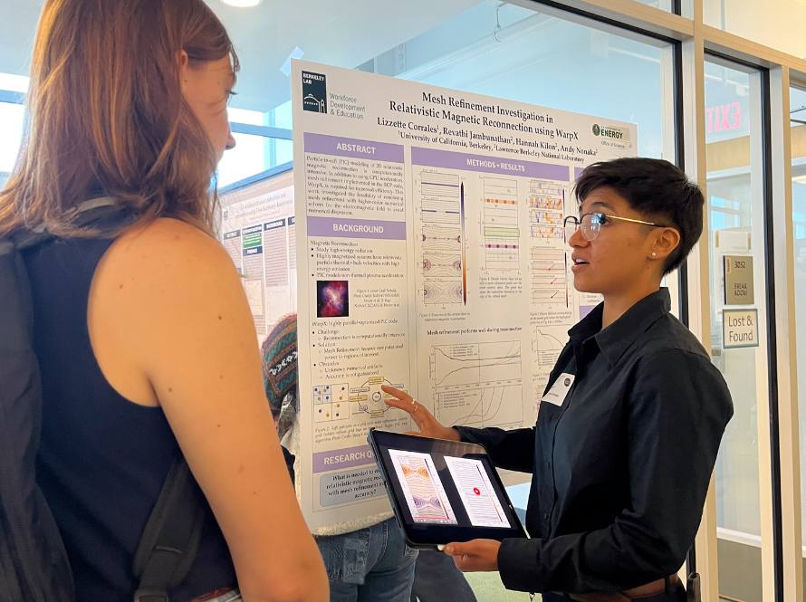 Two Summer Program participants discuss a poster during a poster session, aided by iPad visuals.