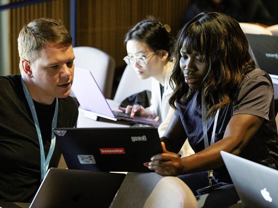 Three young people, a caucasian man, a black woman, and an Asian woman compute together during an event.