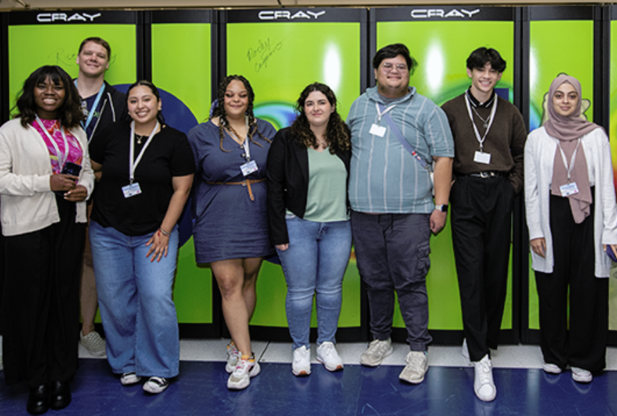 A diverse group of visitors pose in front of the Cori supercomputing cabinet in the NERSC machine room.