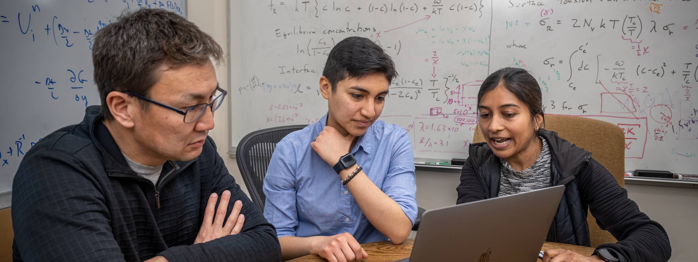 Andy Nonaka works with summer program participant and SULI intern Lisette Corrales in front of white boards with equations and discussing matter on a laptop.