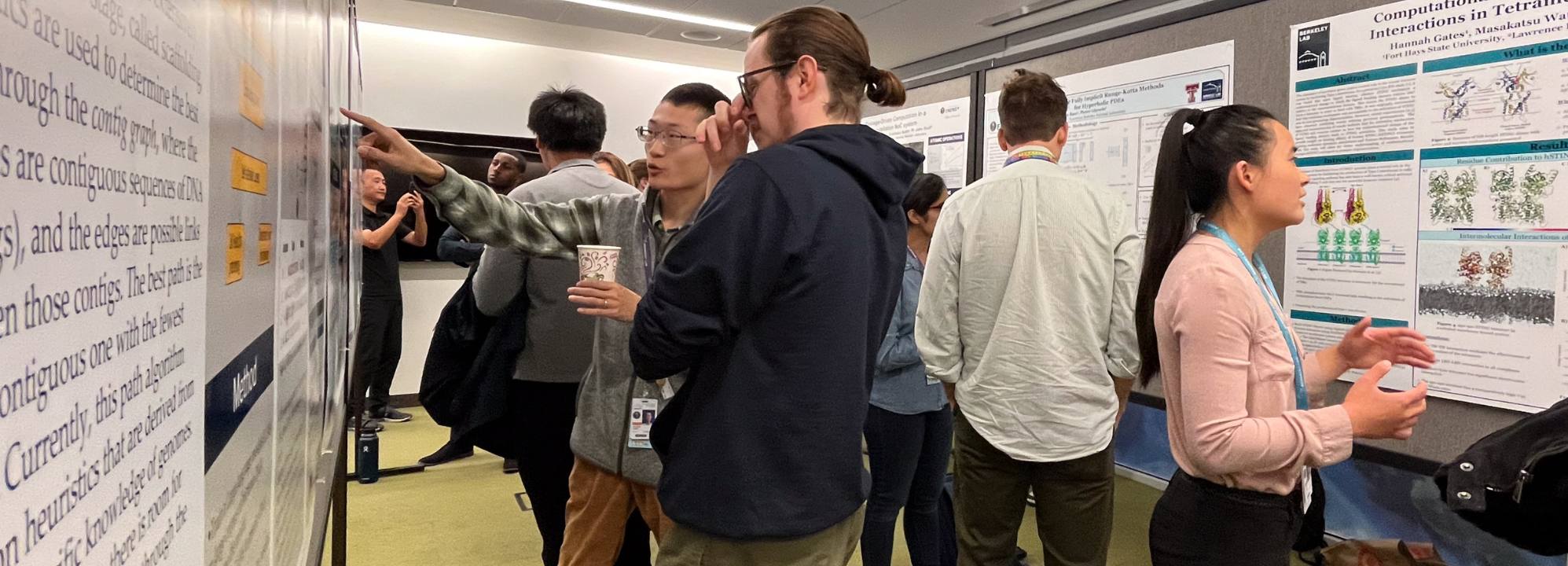 Many summer student participants point at and discuss posters on display.