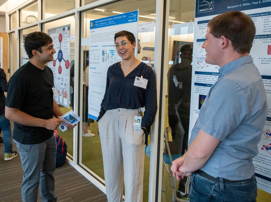 A diverse group of three summer student interns share a chat in front of a wall of science posters.