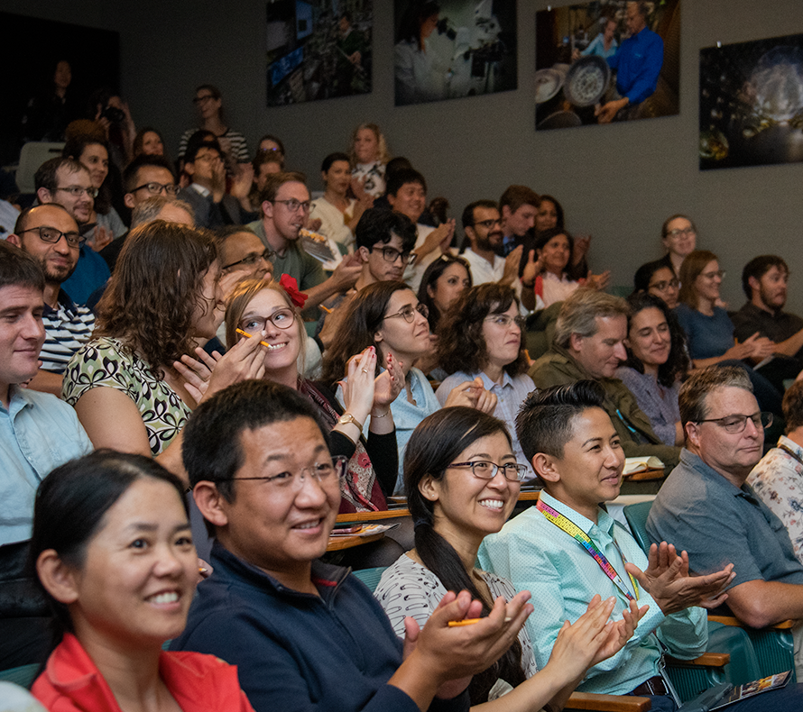 A diverse group of LBNL employees joyfully claps during an assembly.