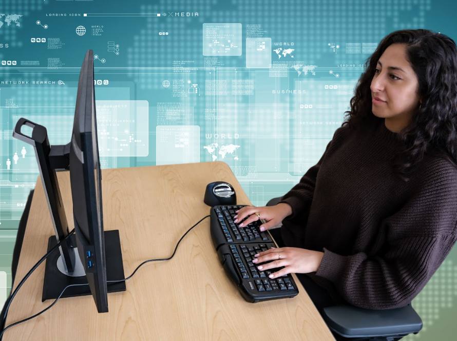 A young woman with medium complexion and long, dark, wavy hair demonstrates proper typing posture at a computer workstation.