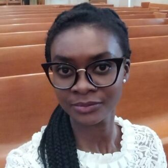 Head shot of Mercy Amankwah, an African-American woman with dark brown complexion, black hair in a ponytail hairstyle, wearing black glasses and a white blouse.