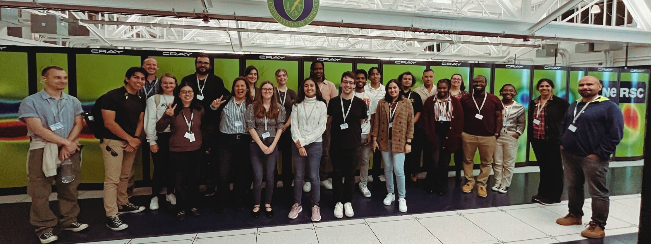 A diverse group of young men and women pose in front of the NERSC's Cori supercomputer.