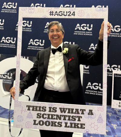 Person in a tuxedo holding up a photobooth sign that says "this is what a scientist looks like."