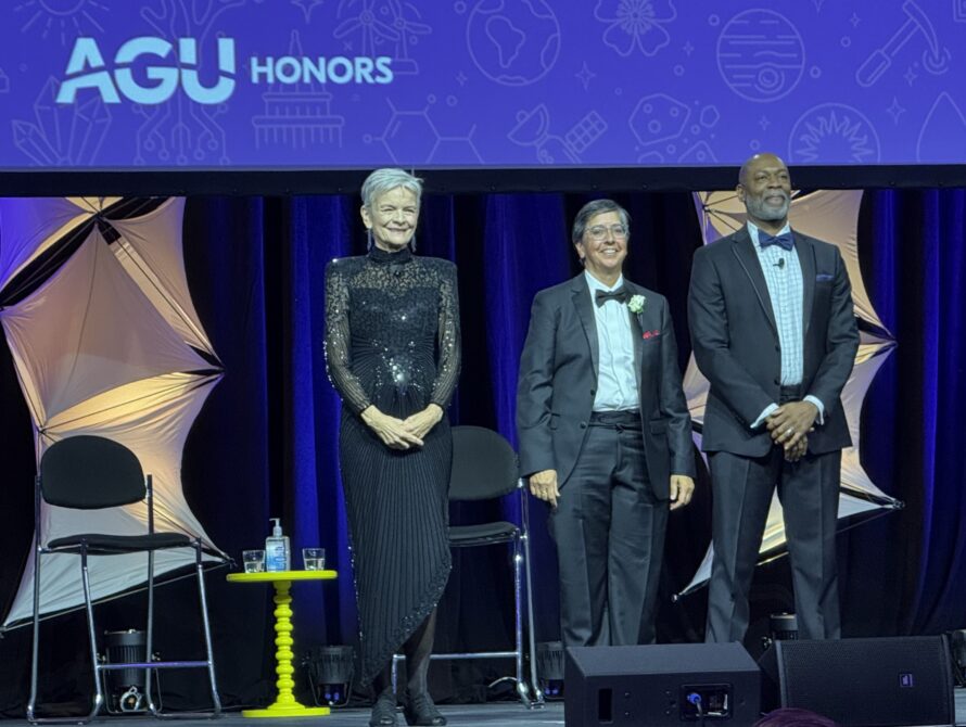 Three people in formal wear standing on an awards stage. Behind them is a purple banner that says AGU.