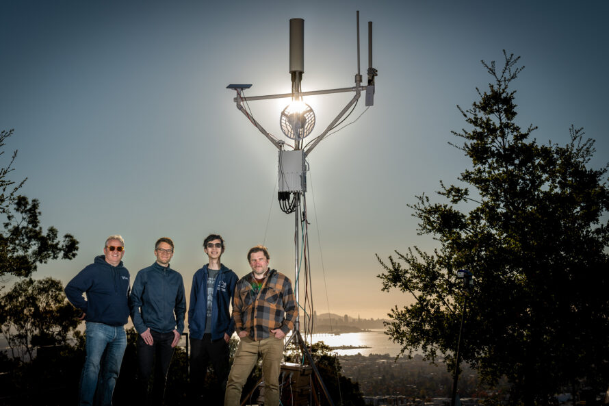 Four men in front a wireless tower with a setting sun behind them