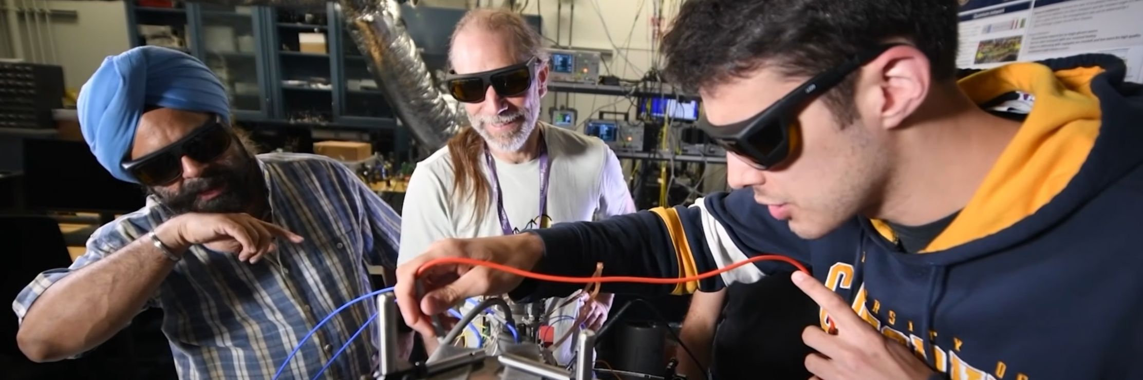 Three people wearing protective eye glasses working on electrical equipment.