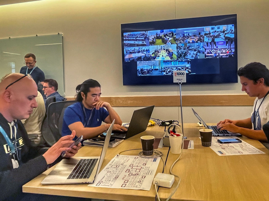 Several people enter prompts on their laptops in front of a Zoom screen displaying other participants across the United States during the AI Jam event.