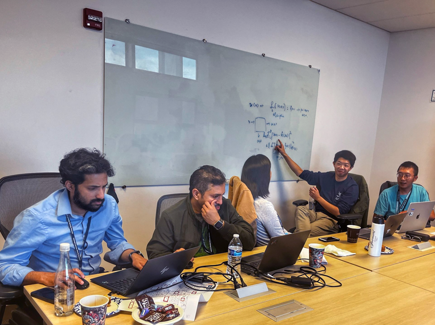 Five people gathered around a conference table and a large white board during the AI Jam event