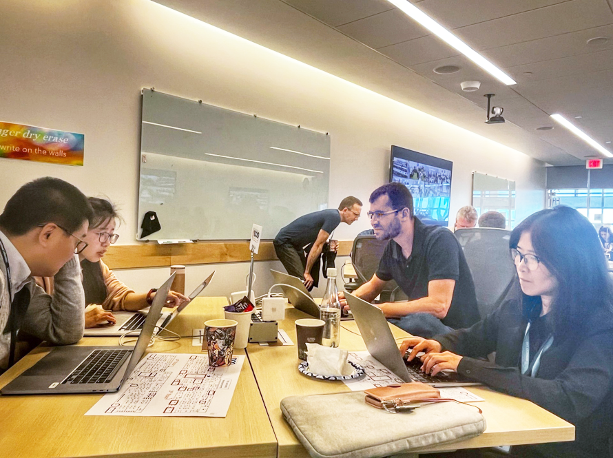 Several people enter prompts on their laptops during the AI Jam event.