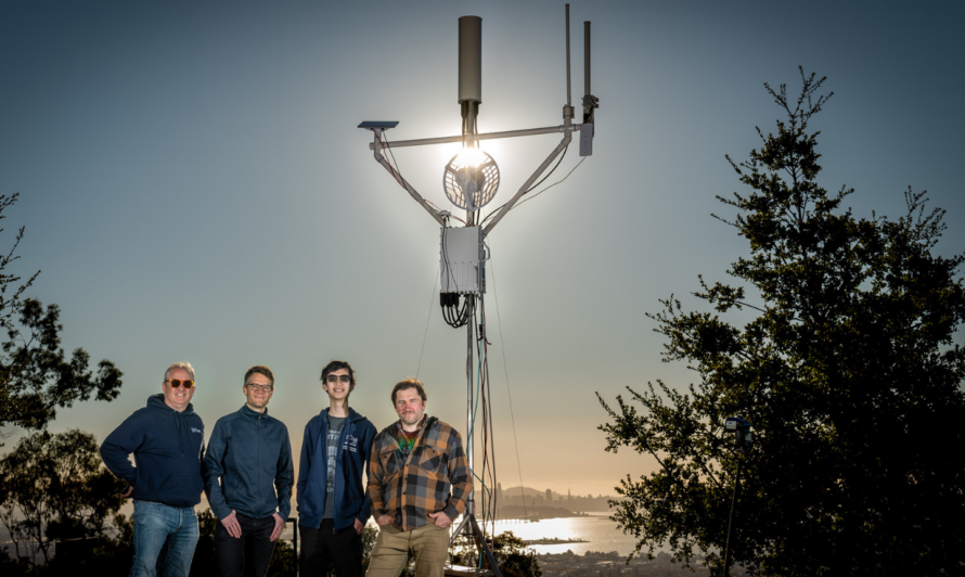 Four men in front a wireless tower with a setting sun behind them.