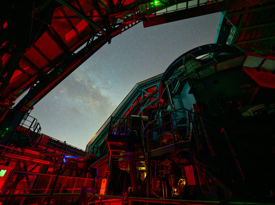 Photo of the interior of the Simonyi Survey Telescope with red light in the dome and a starry twilight sky outside.