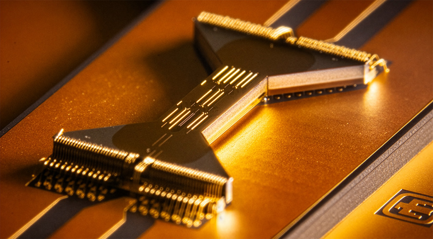 Close-up view of a gold-coated quantum processor chip with intricate wiring and connectors, illuminated by warm light.