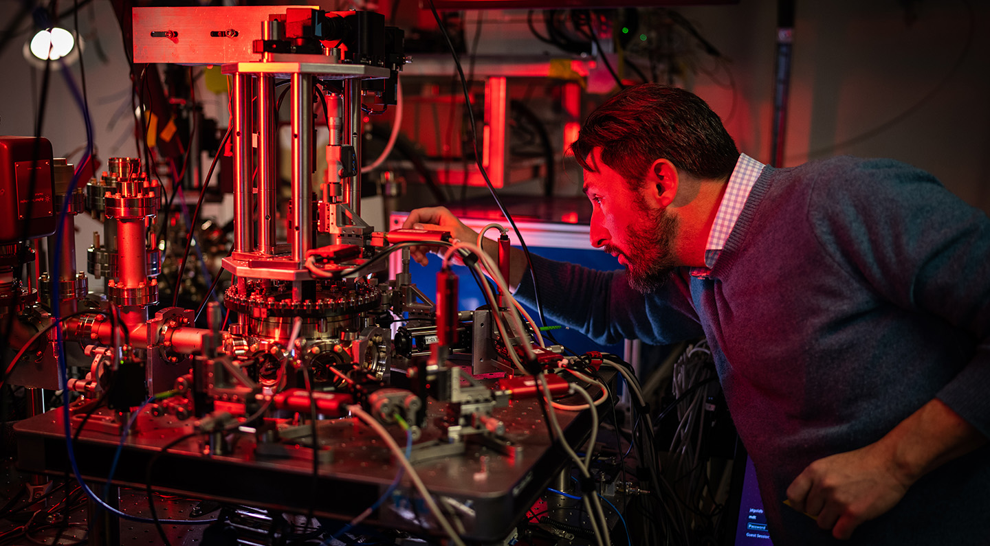 Person working with a complex setup of scientific equipment in a laboratory filled with wires, metal components, and glowing red lights.