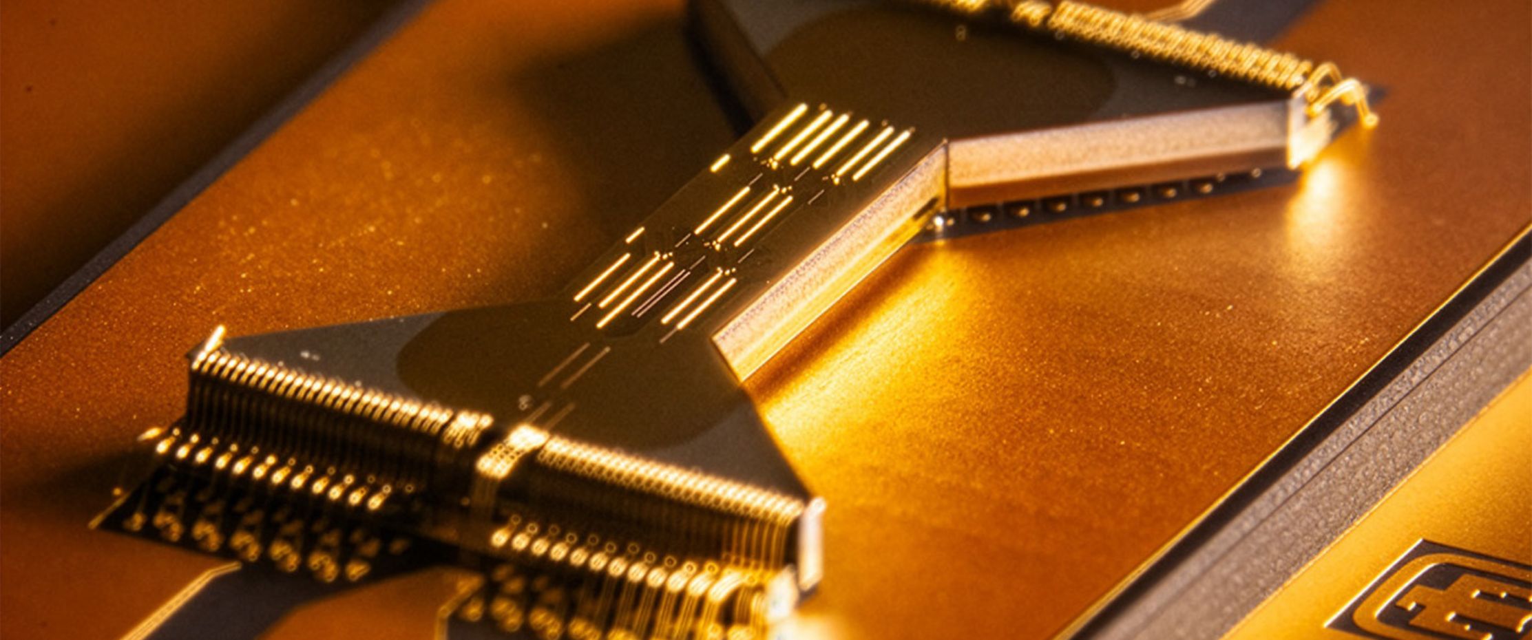 Close-up view of a gold-coated quantum processor chip with intricate wiring and connectors, illuminated by warm light.
