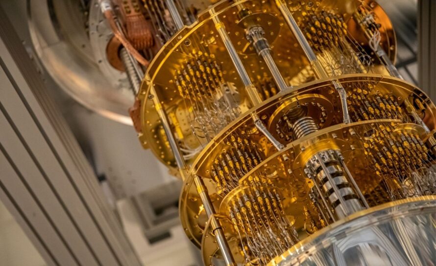 Close-up view of a quantum computer’s superconducting processor housed within a cylindrical, gold-colored cryogenic chamber, featuring multiple stacked plates connected by intricate wiring and metallic rods.