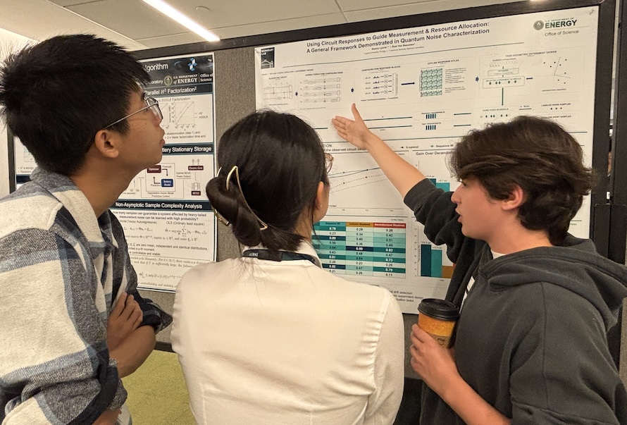 Three summer interns discuss a science poster by viewing and pointing to a large print-out mounted on a bulletin board.