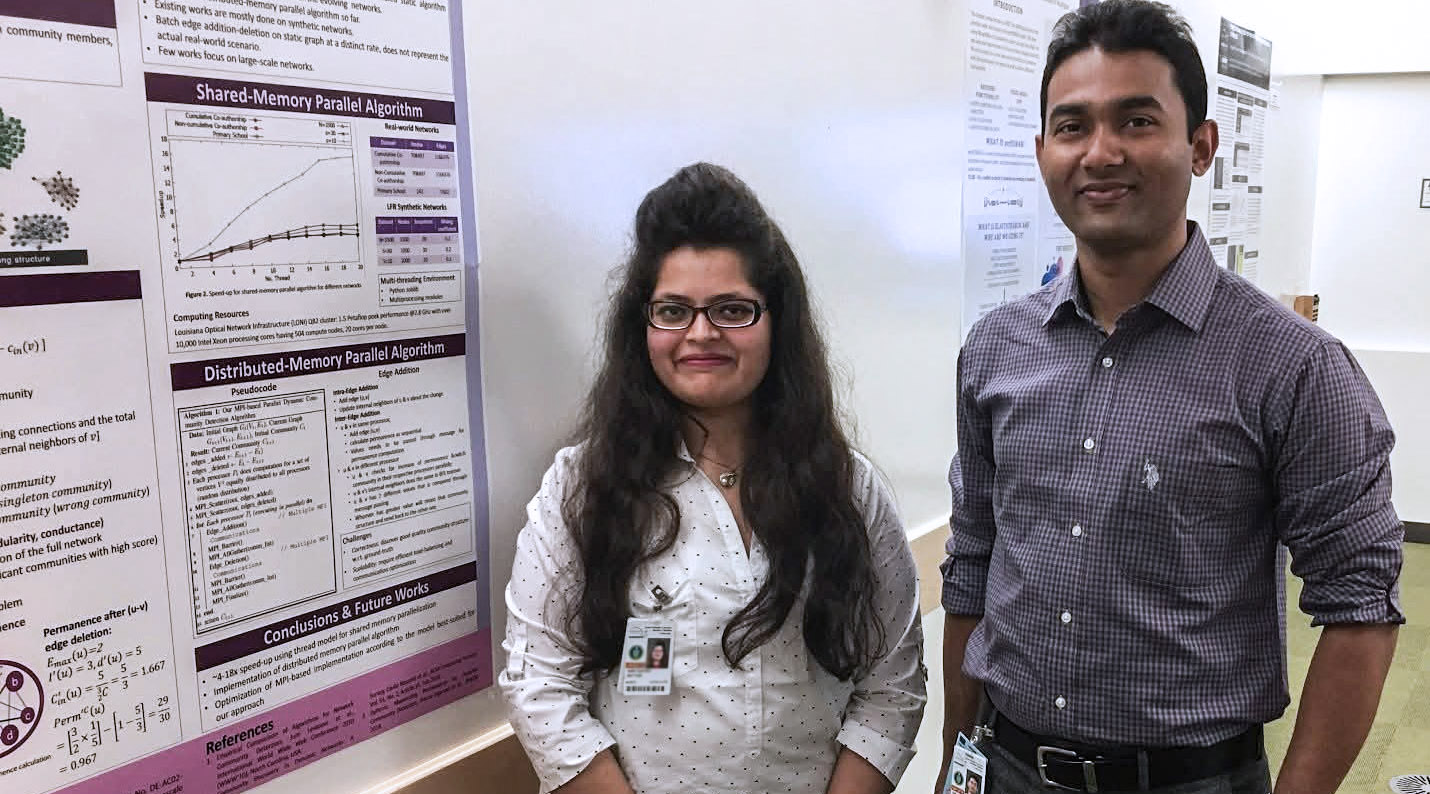 Naw Safrin Sattar and Shaikh Arifuzzaman stand side-by-side smiling at the camera in front of a large, detailed scientific research poster. Sattar, on the left, has long dark hair and wears glasses and a white dotted button-down shirt. Arifuzzaman, on the right, wears a purple checkered button-down shirt. Both are wearing laboratory ID badges on lanyards. The poster behind them features charts, graphs, and sections titled "Shared-Memory Parallel Algorithm" and "Distributed-Memory Parallel Algorithm."